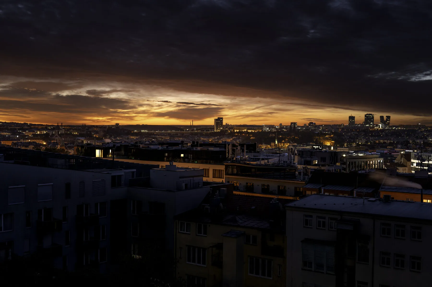 A thin band of fire under heavy cloud over the rooftops.
