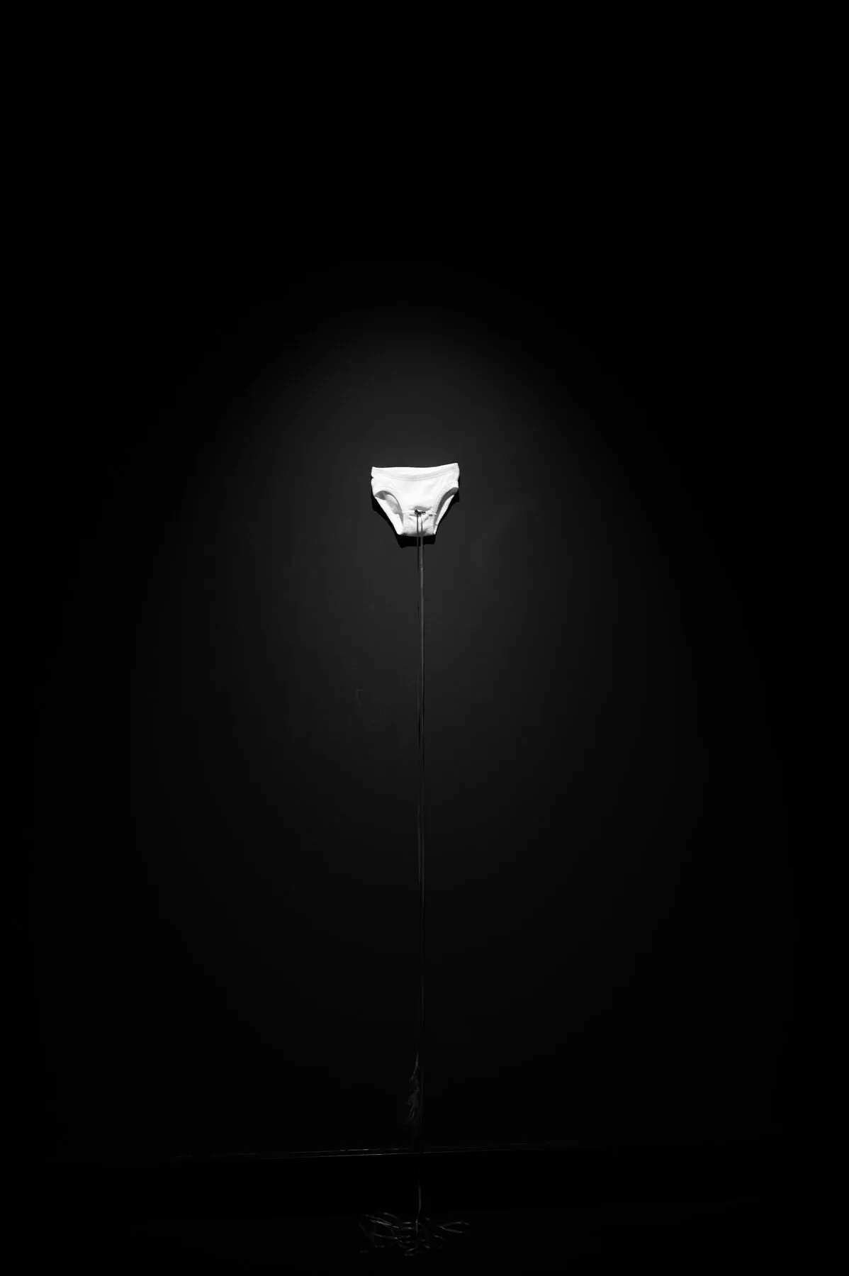 White briefs on a thin line, one spotlight, a sea of black.