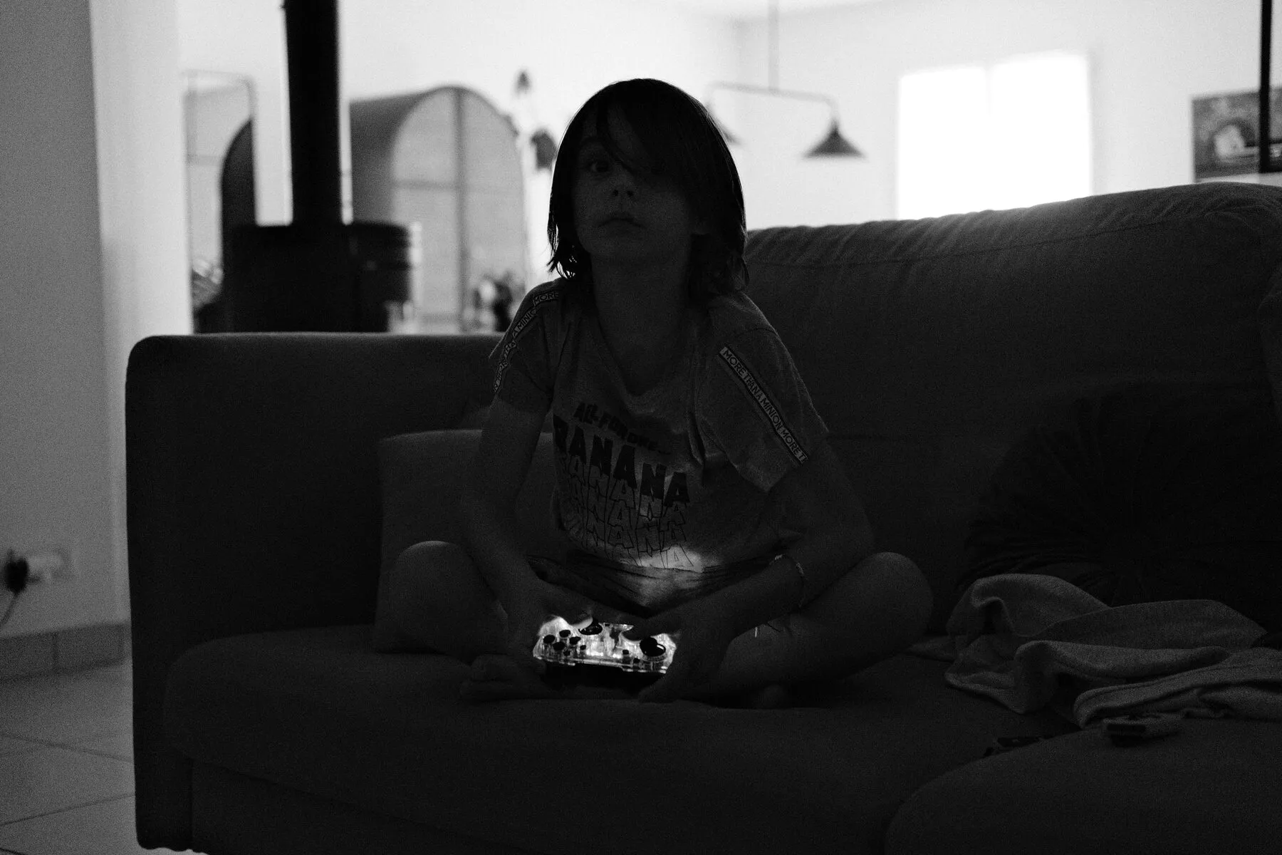 A child cross-legged on the sofa lit only by a game controller.