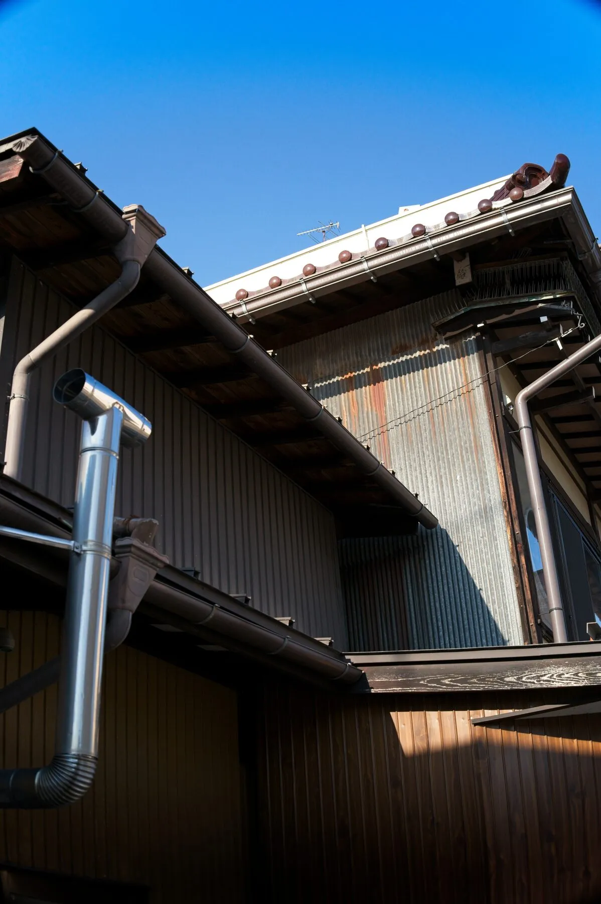 House eaves and a bright galvanised downpipe against deep blue.
