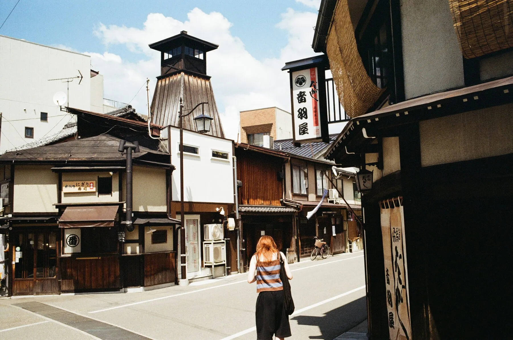 A woman walks away toward the old fire-lookout tower, blue sky.