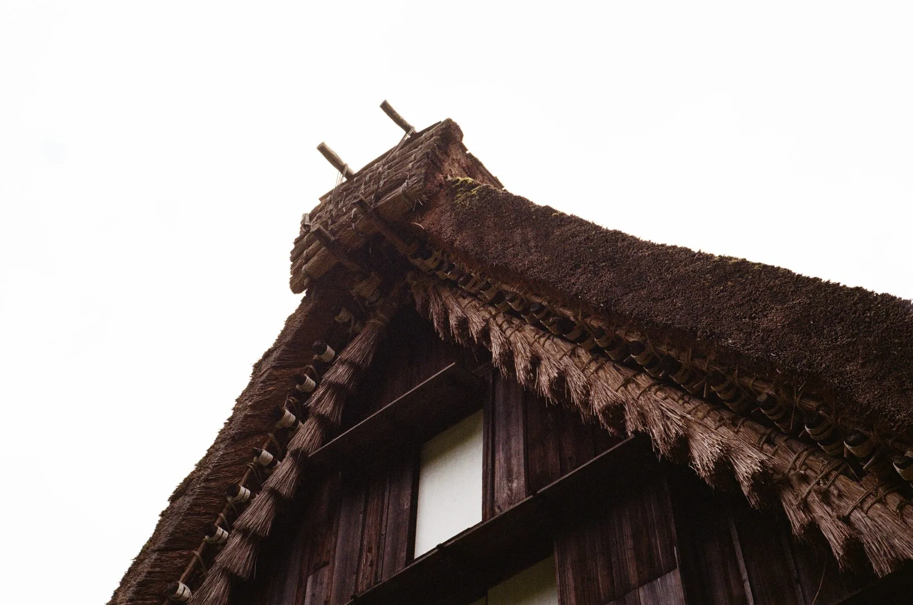 The thatched gable of a gassho-zukuri house against white sky.