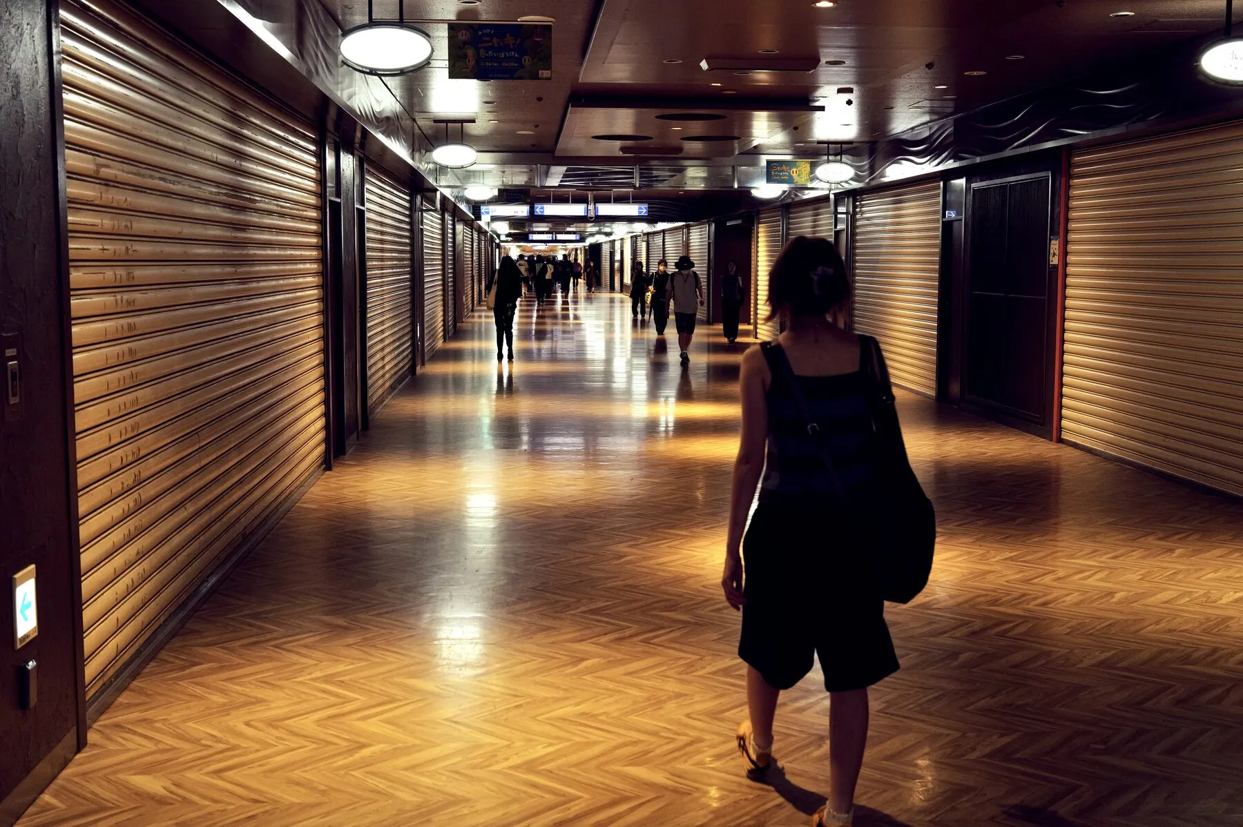 A woman down a warm herringbone-floored underground arcade, shops shut.