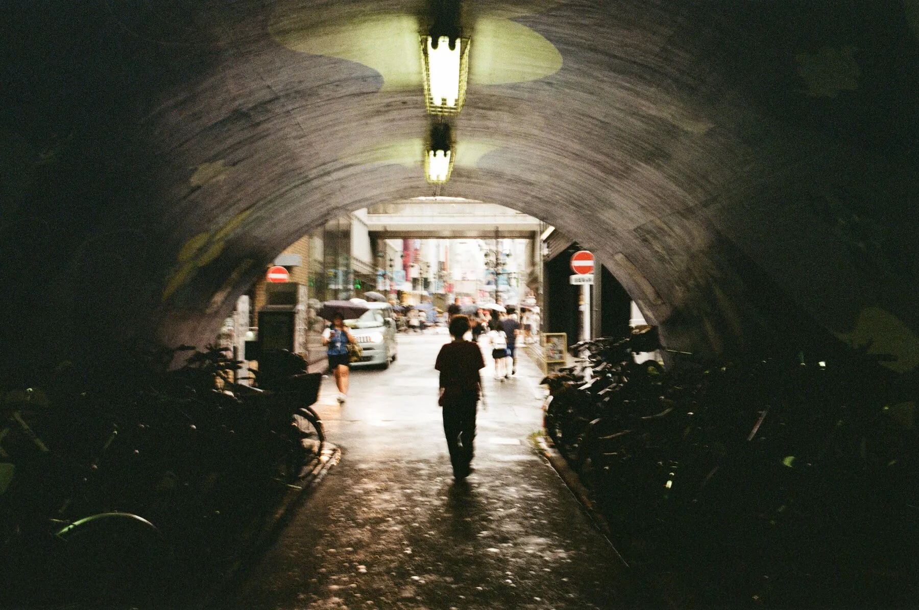 A silhouette in a lamp-lit pedestrian tunnel, shopping street beyond.