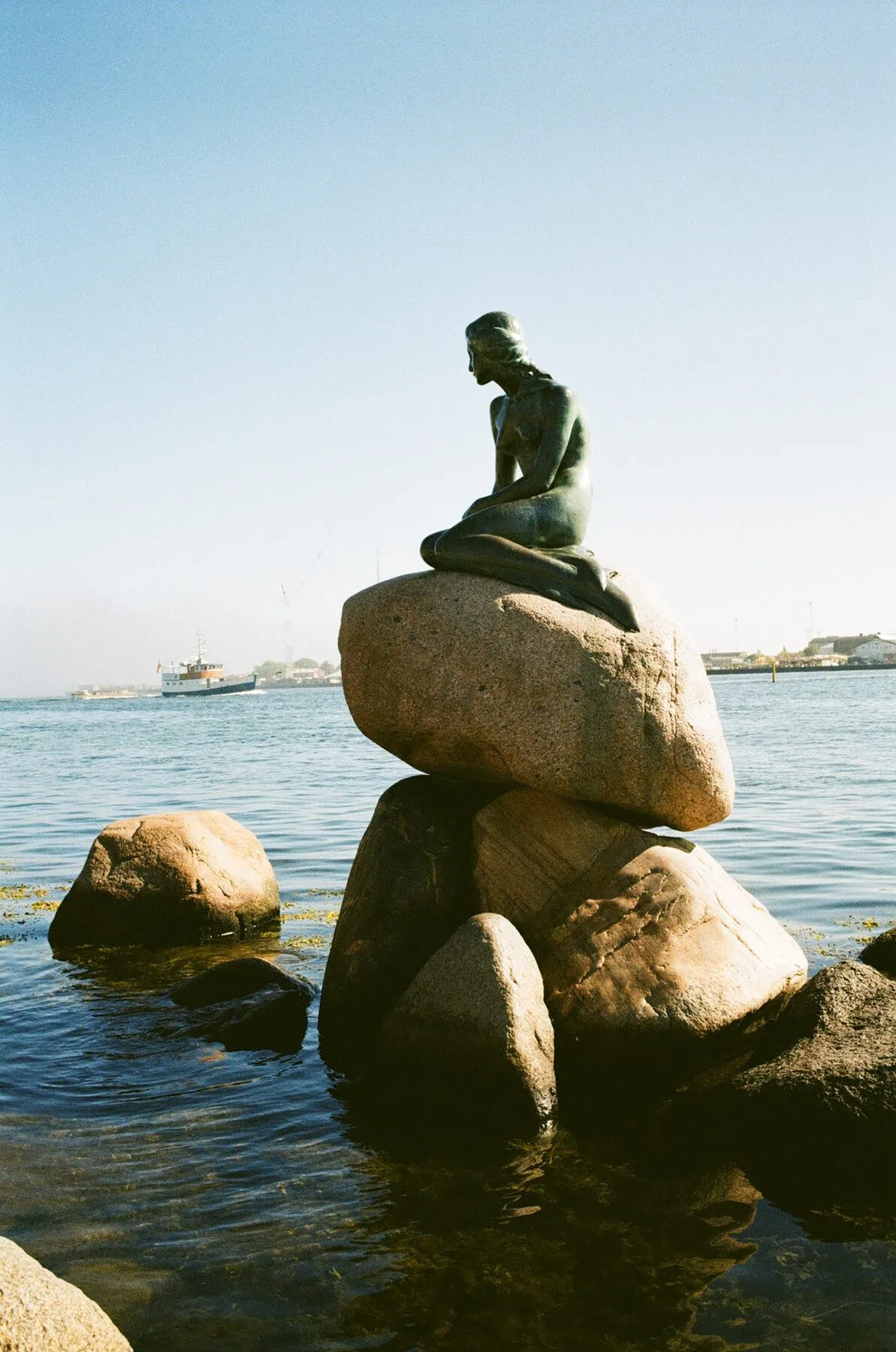 The Little Mermaid on her rock, a ship on the sea behind.