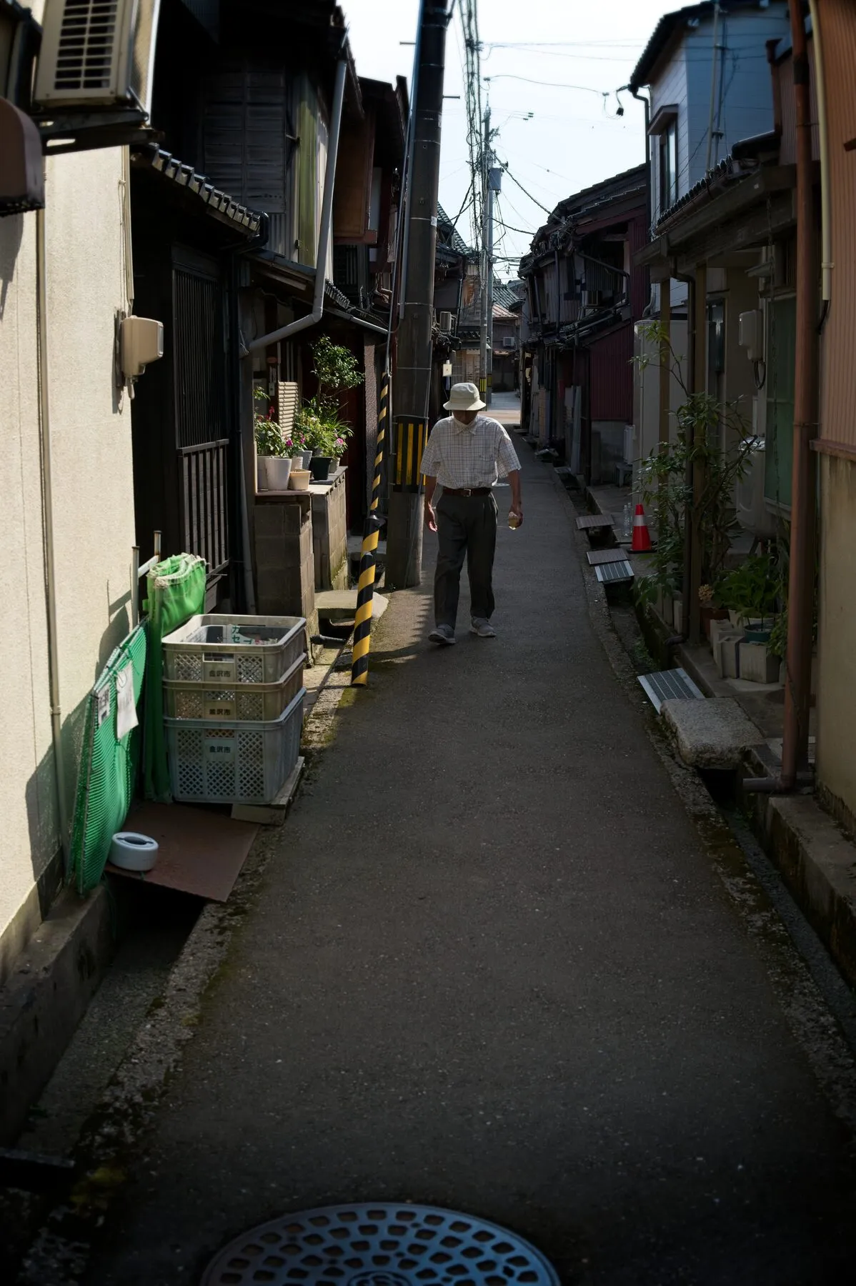 An old man in a hat walks toward the camera down a narrow lane.
