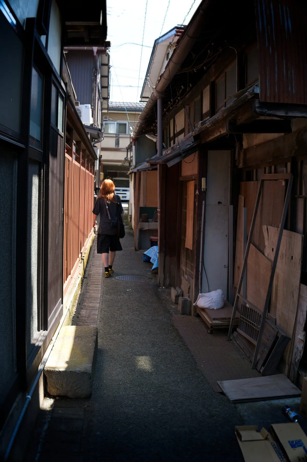 An orange-haired figure walks away down a sharp-shadowed alley.