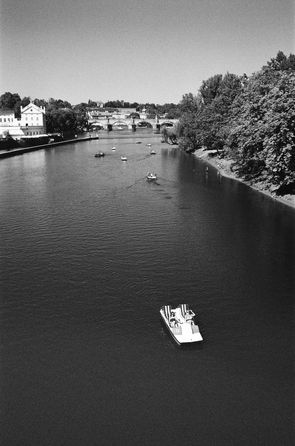 A pedal boat on the sunlit river seen from the bridge.