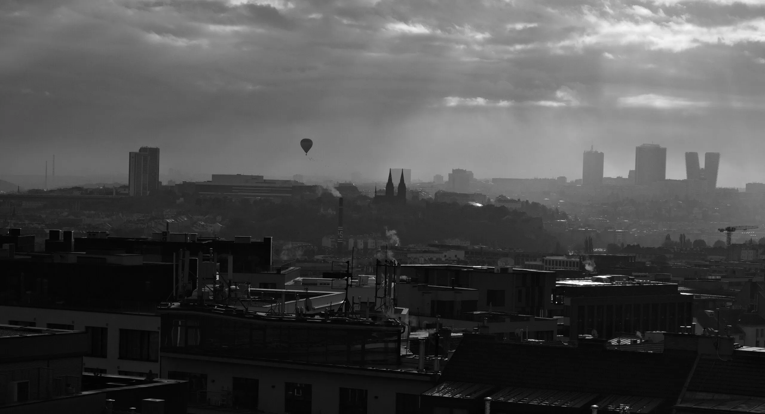 A hot-air balloon over a hazy skyline pierced by god-rays.