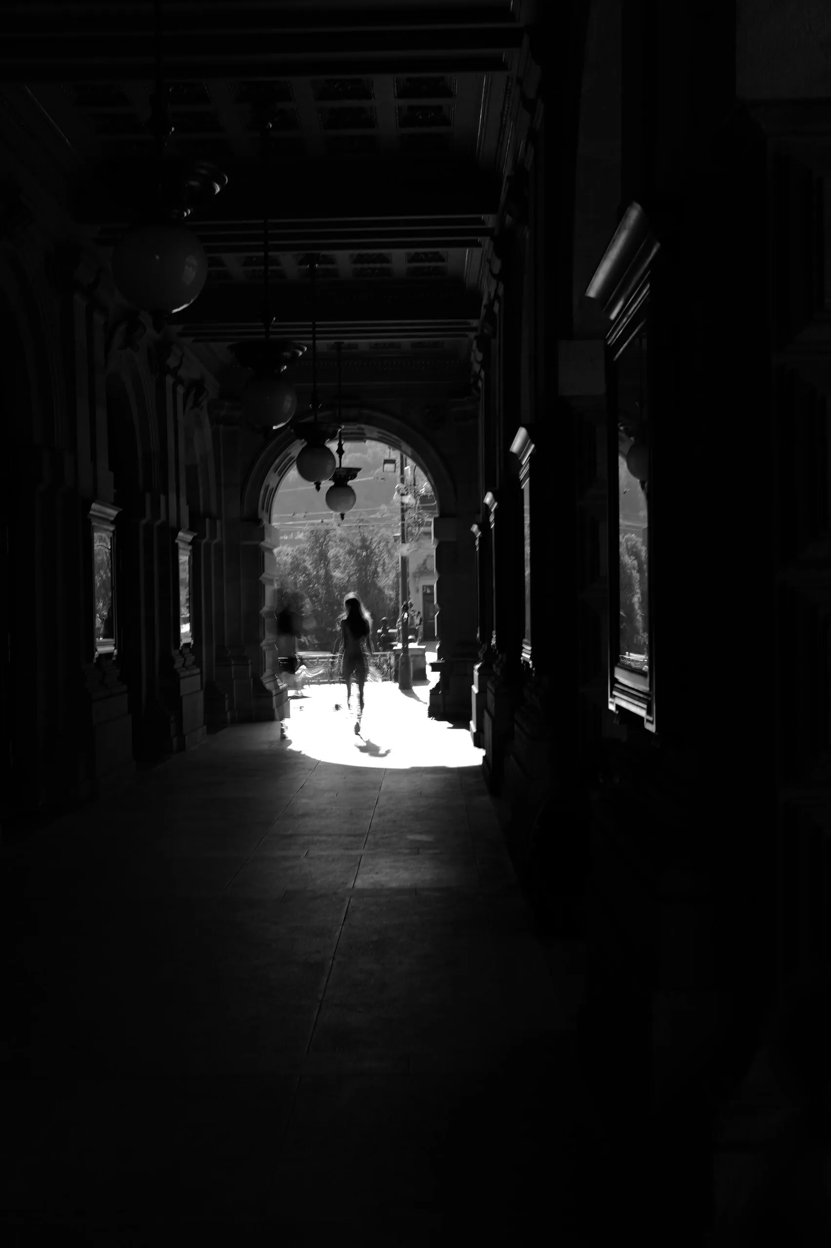 A figure crossing a bright sunlit patch inside a dark colonnade.