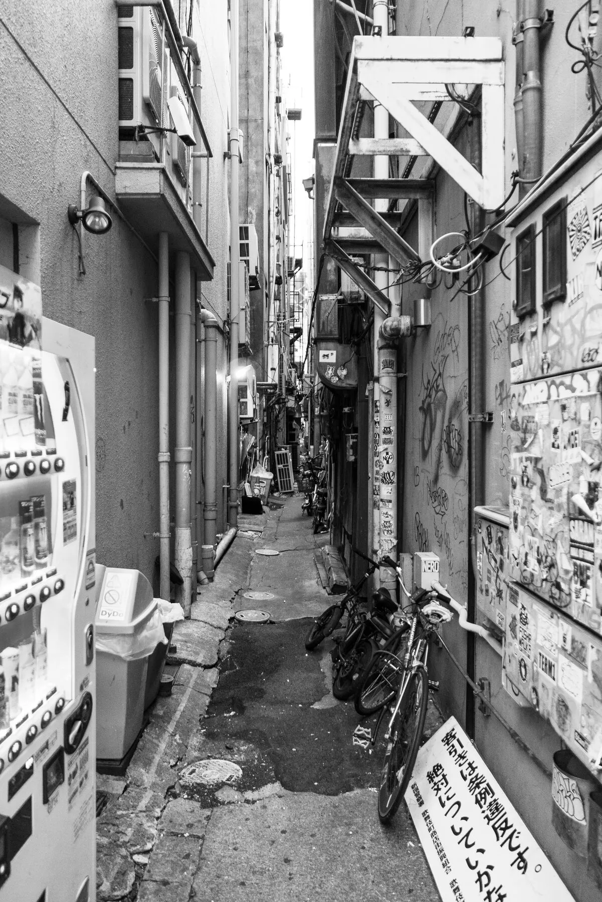A vending machine and bikes in a razor-thin alley.