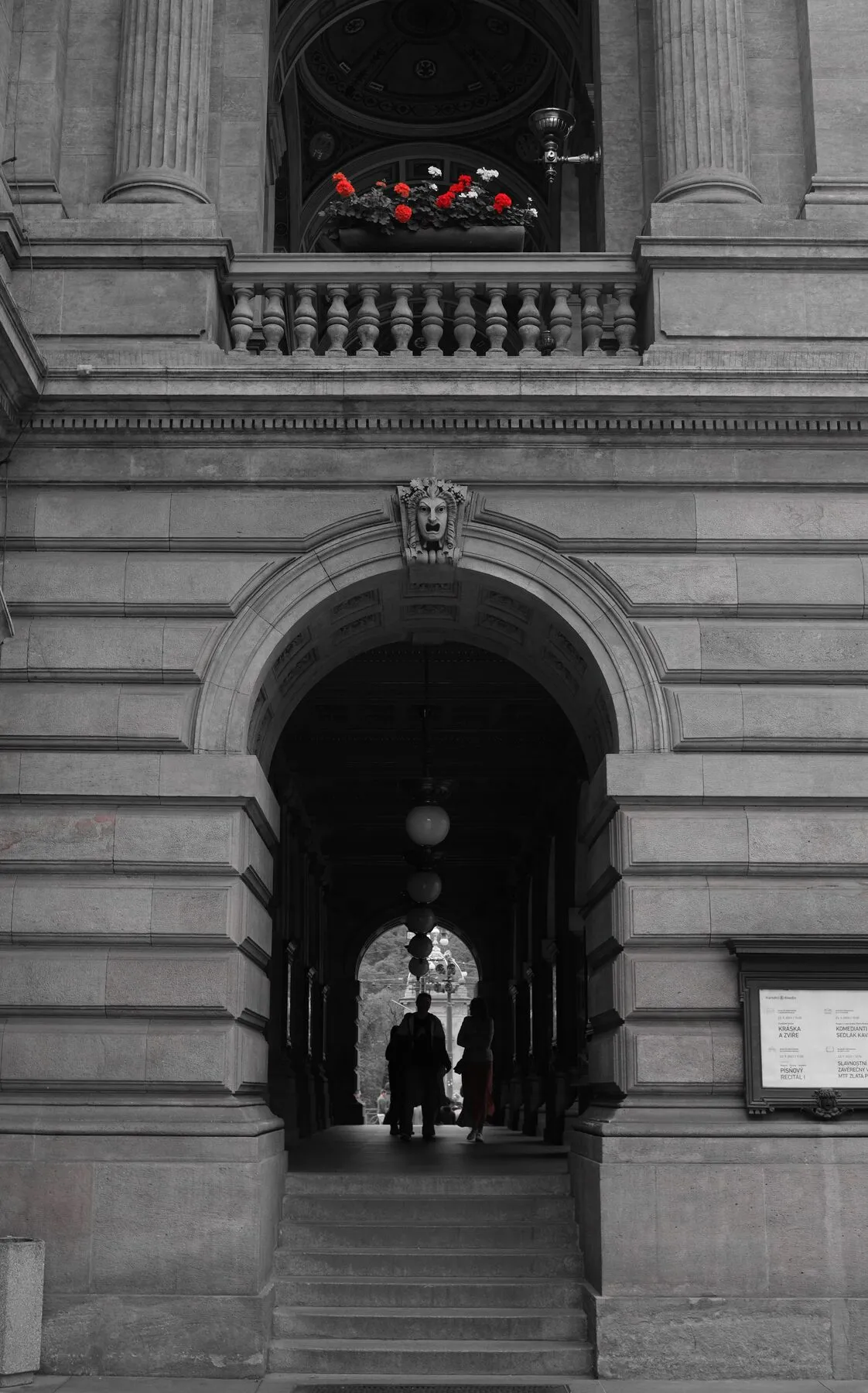 Selective colour: red flowers and a silhouetted couple in a grey arch.