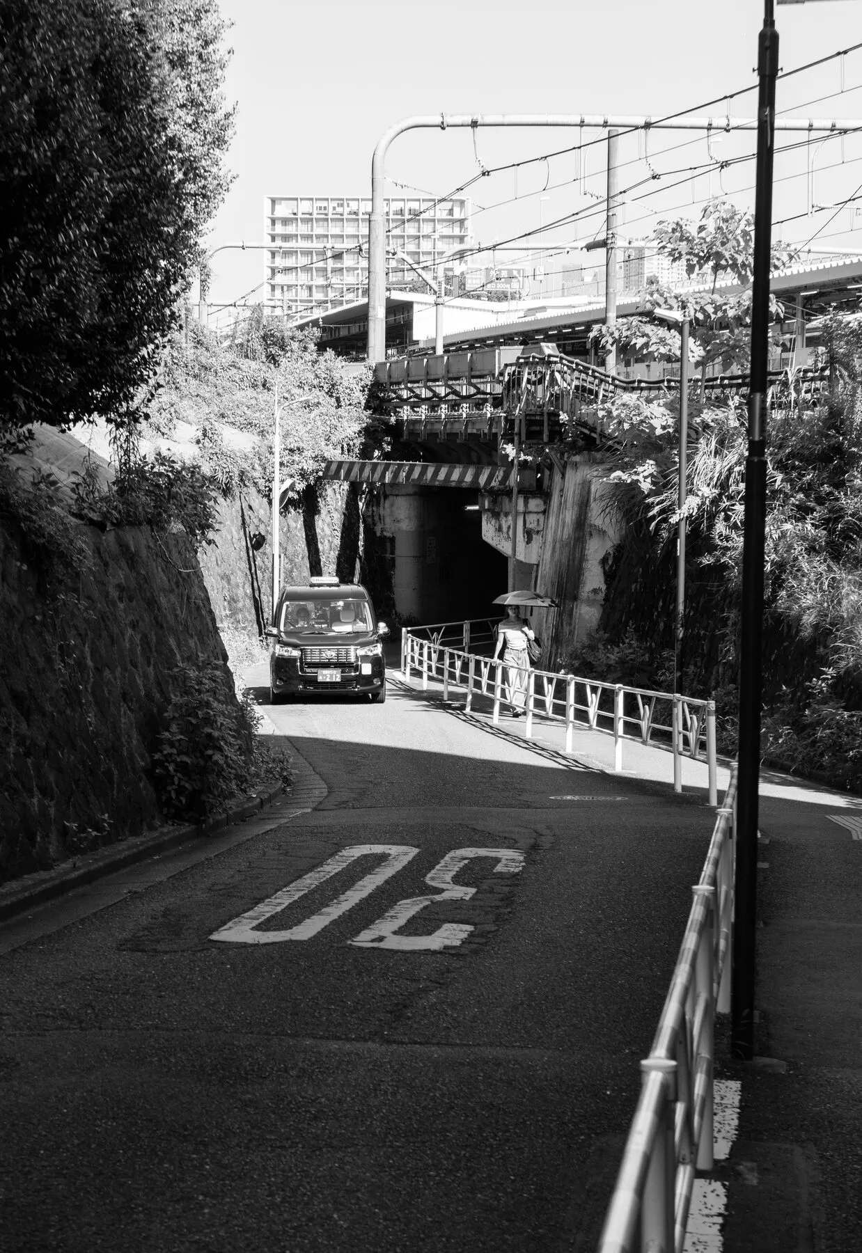 A giant '30' road marking, a taxi, a parasol under the railway bridge.