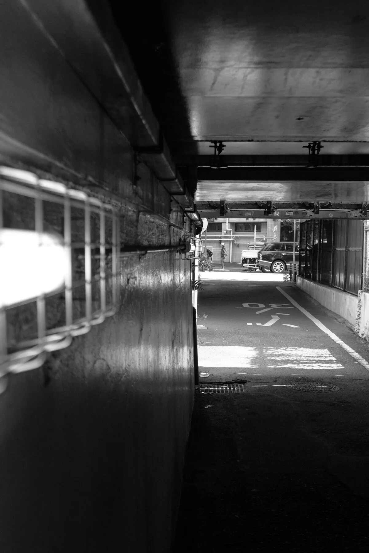 Side light on a textured wall, a car and cyclist at the tunnel end.