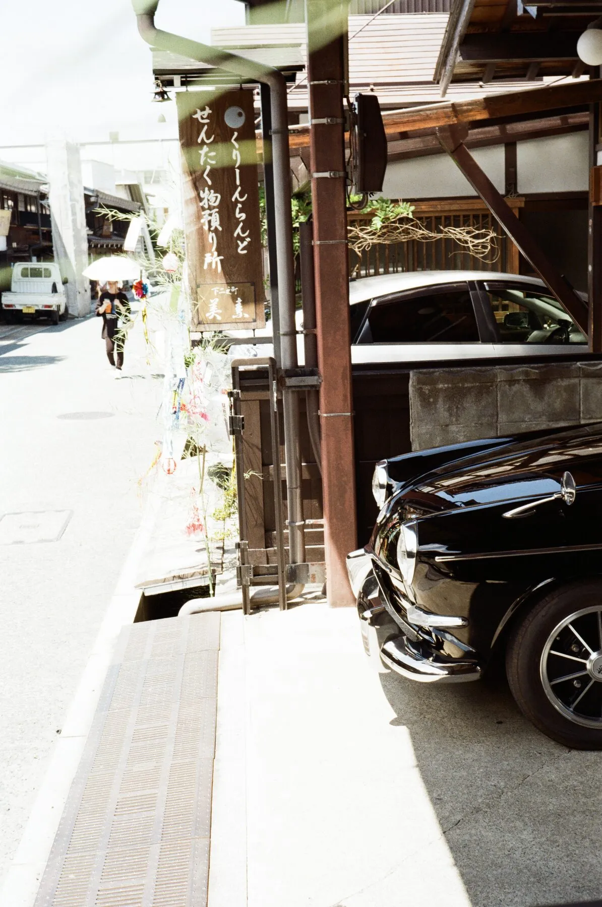 Glossy black vintage cars parked under the eaves in hard sun.